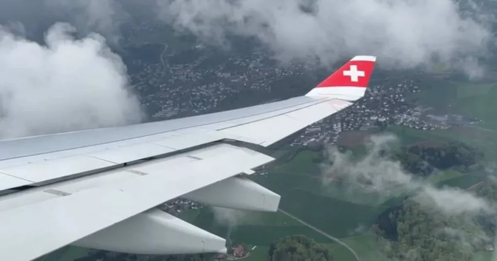 Airplane with with Swiss logo surrounded by clouds with Swiss town below